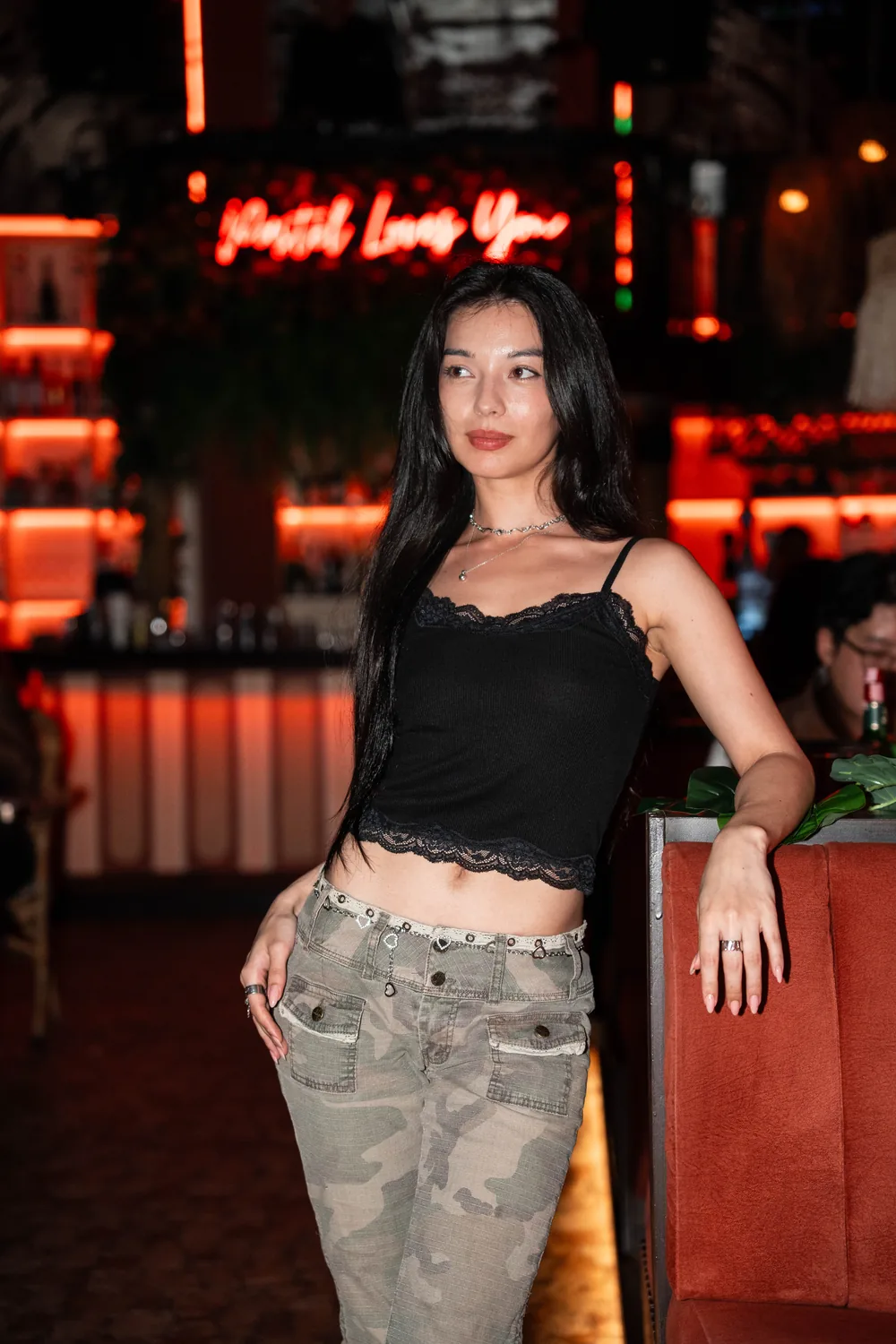Modèle en top noir et pantalon camouflage devant une enseigne néon rouge