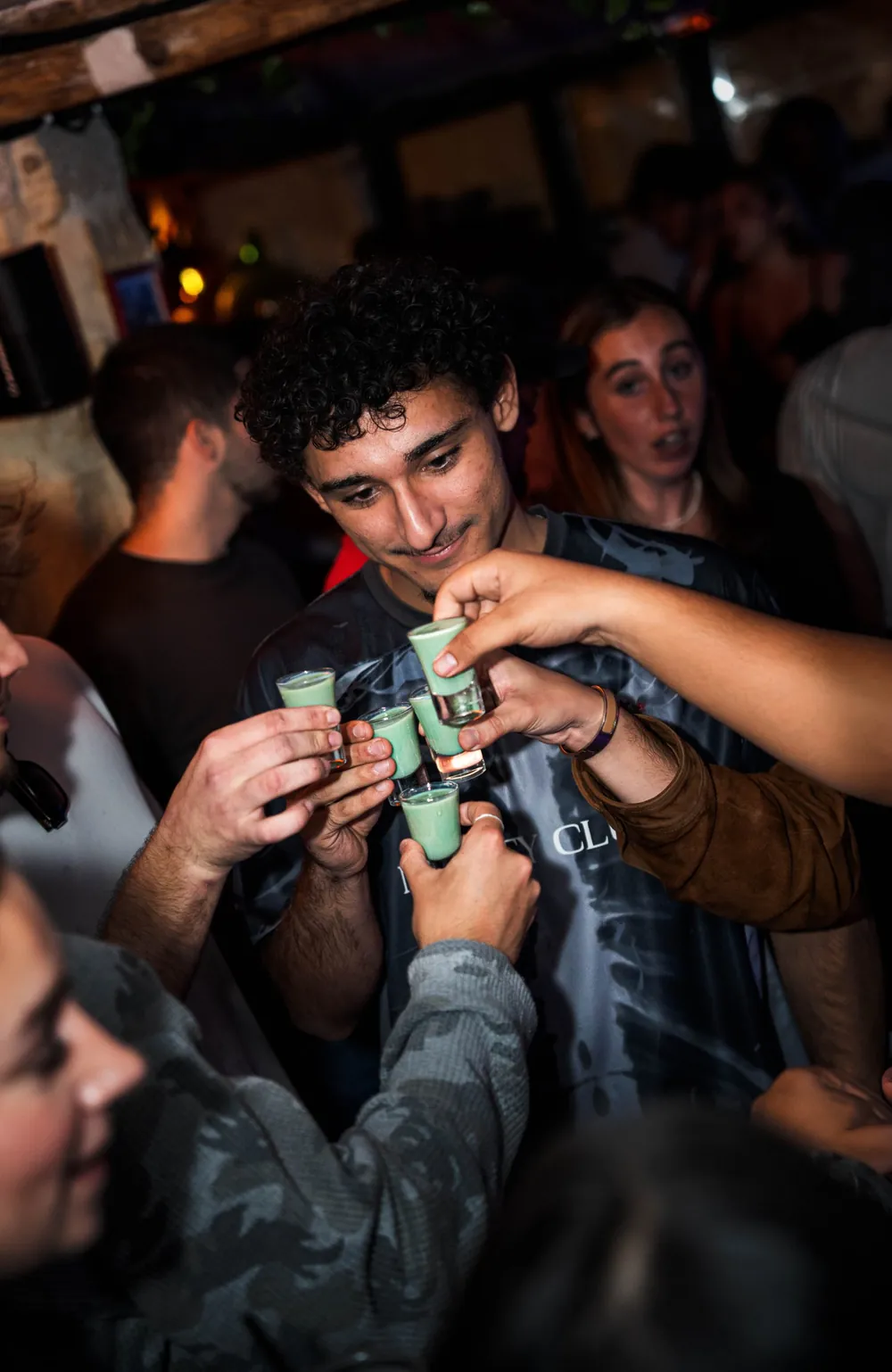 Groupe d'amis trinquant avec des shots verts au milieu de la foule d'un bar